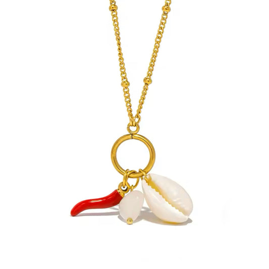 Close-up of red Italian cornicello charm and cowrie shell on gold necklace